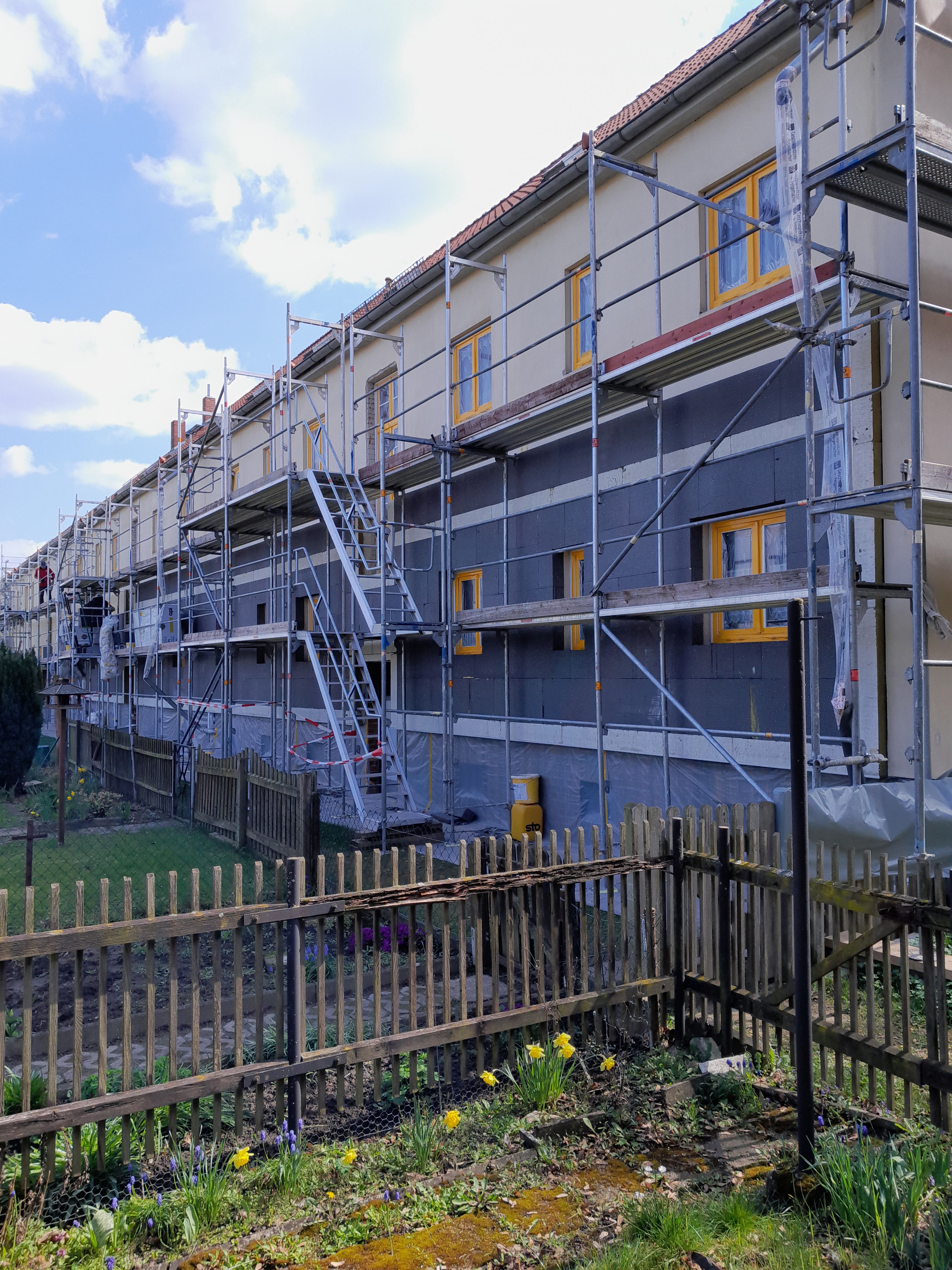 Baustelle mit Rohbau eines Mehrfamilienhauses und Baugerüsten dahinter die graue Dämmung