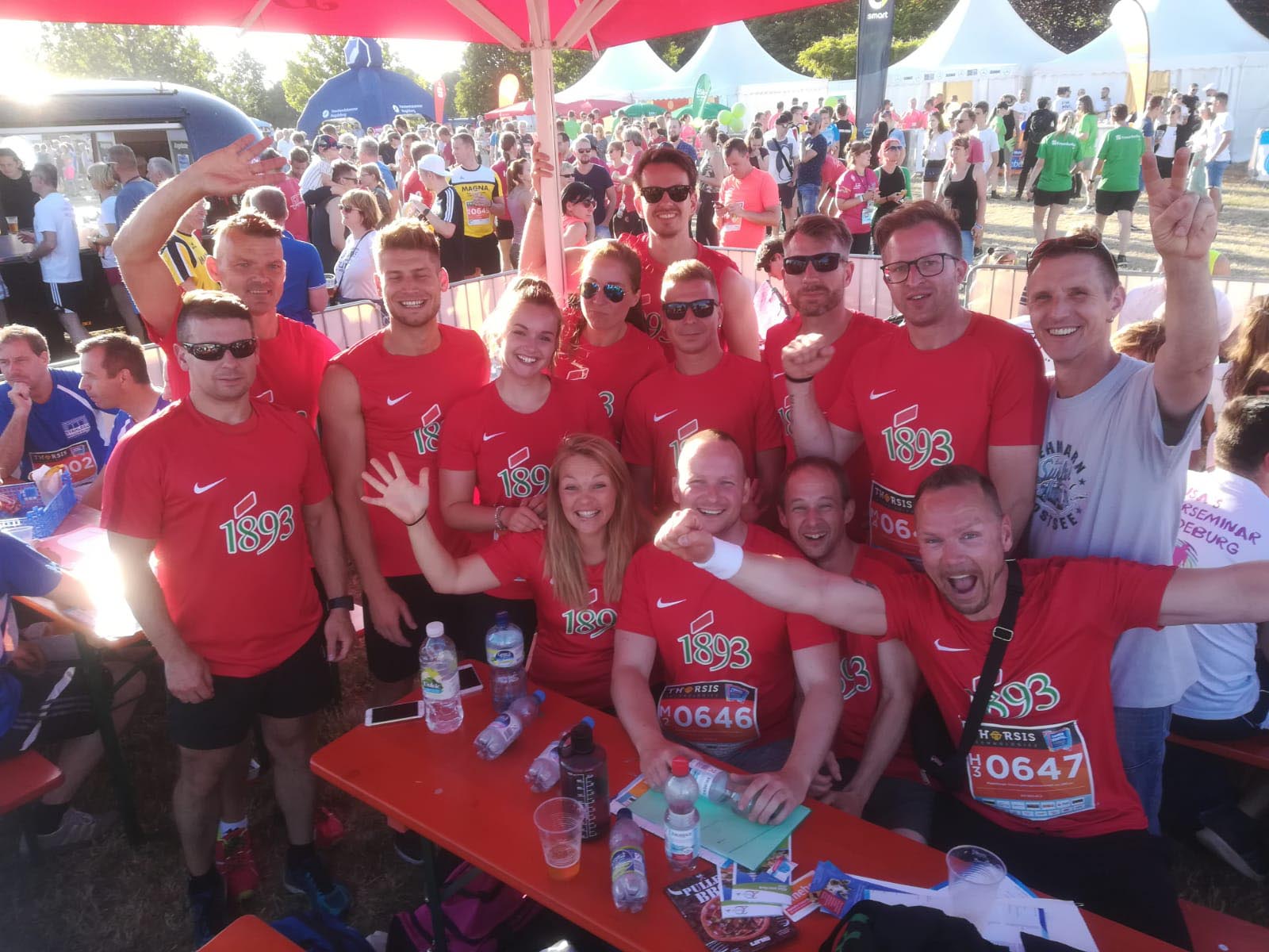 Mitarbeiter der 1893 tragen rote Lauftrikots und jubeln in die Kamera