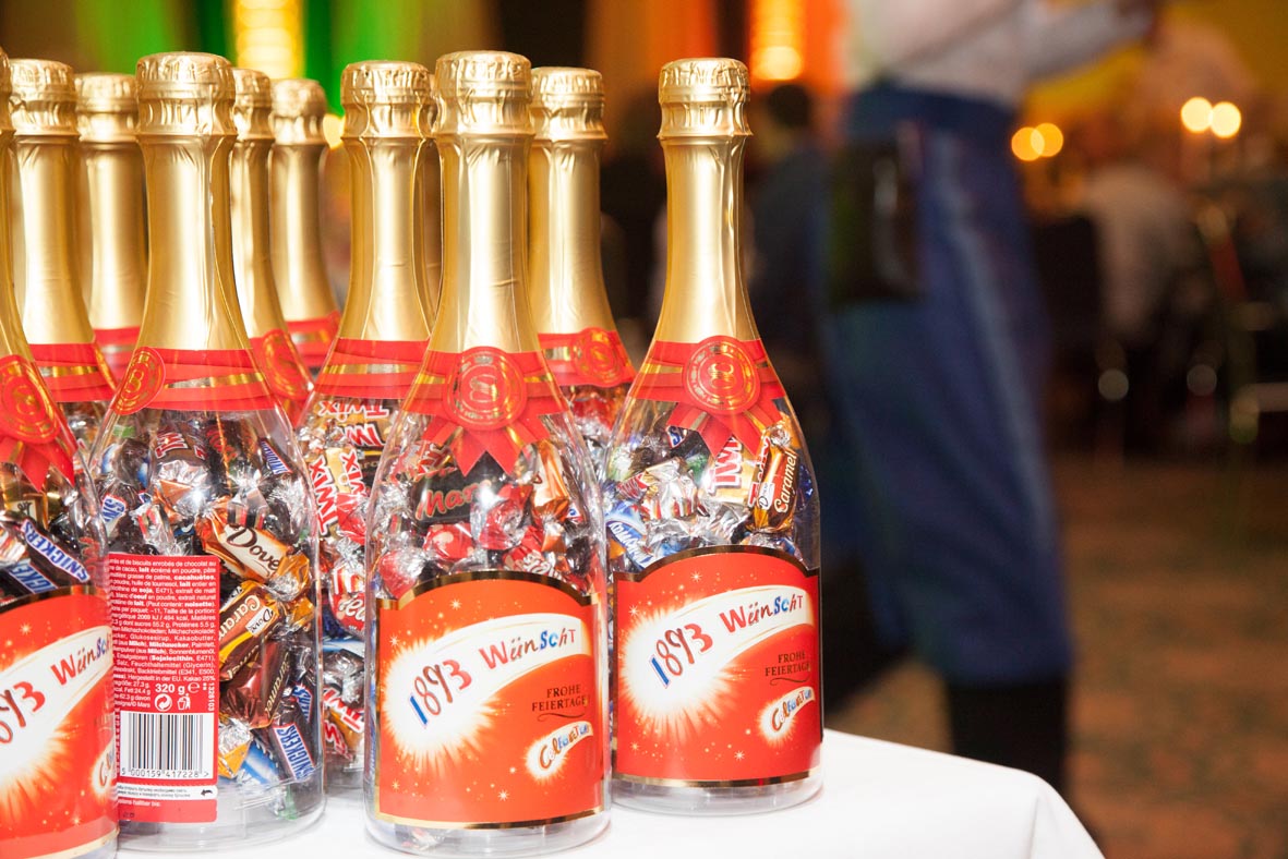 Auf einem Tisch mit weißer Tischdecke stehen Sektflaschen gefüllt mit Schokolade