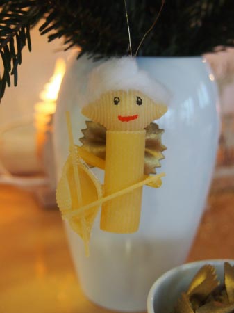 Ein gelber selbstgebastelter Weihnachtsengel vor einer Vase mit Tannengrün