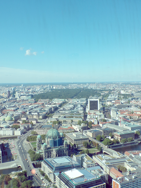 Die Aufnahme zeigt ein Panorama der Berliner Innenstadt aus großer Höhe. Im Vordergrund ist der Berliner Dom zu sehen, dahinter erstrecken sich der Große Tiergarten und zahlreiche Gebäude des Stadtzentrums