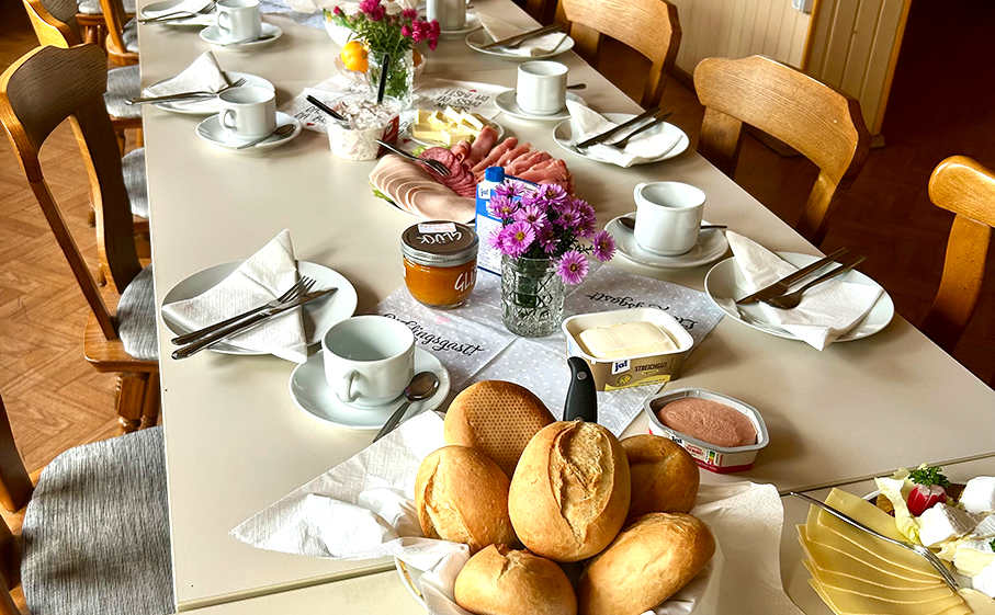 Vorbereitete Frühstückstafel mit frischen Brötchen, herzhaften Speisen und Blumen bei einer Veranstaltung der 1893.