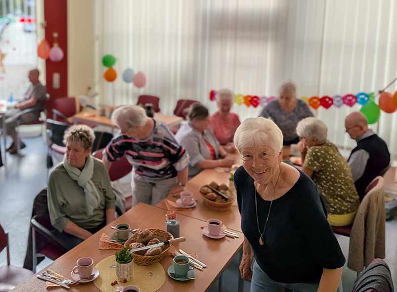 Mehrere Personen treffen sich in einem geschmückten Gemeinschaftsraum zu einem gemeinsamen Frühstück an gedeckten Tischen.