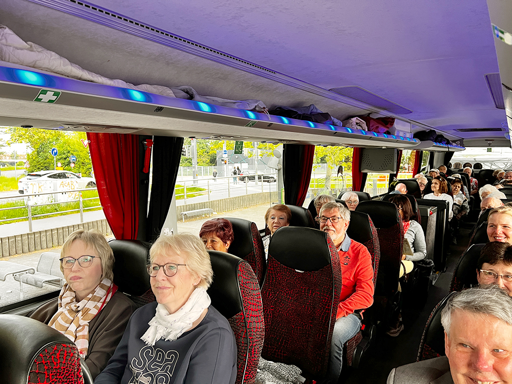 Mehrere Personen sitzen auf den Sitzplätzen eines Reisebusses. Der Gang und die Sitzreihen des Busses sind sichtbar.